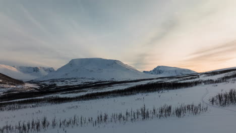 dynamic aerial shot of a landscape full of snow at orange sunset