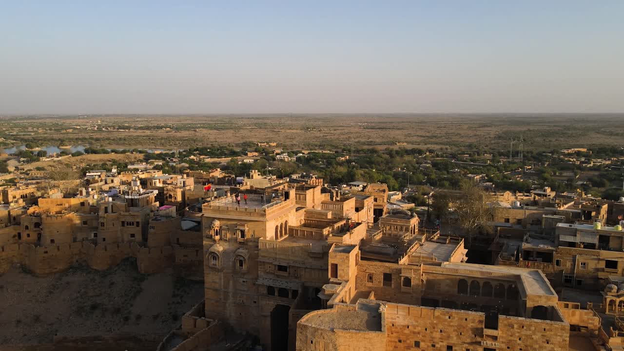 Aerial drone shot capturing Jaisalmer Fort glowing in warm sunset light against the Thar Desert skyline.