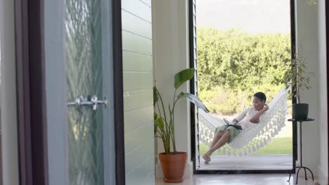 Happy-african-american-woman-sitting-in-hammock-on-terrace,-writing-in-notebook,-slow-motion