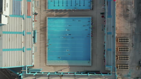 Vista-épica-Del-Entrenamiento-De-Nadadores-Haciendo-Carriles-En-Una-Piscina-Azul-Bajo-El-Sol,-9-De-Septiembre-De-2020