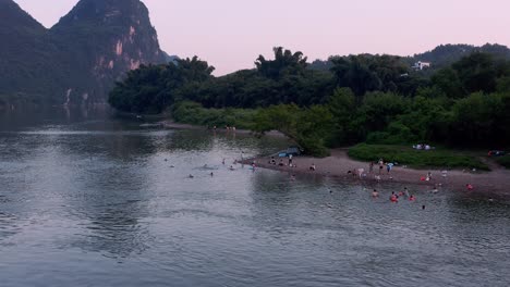 Gente-Bañándose-En-Una-Playa-Aislada-Del-Río,-Paisaje-De-Montaña-Kárstica-De-China,-Antena