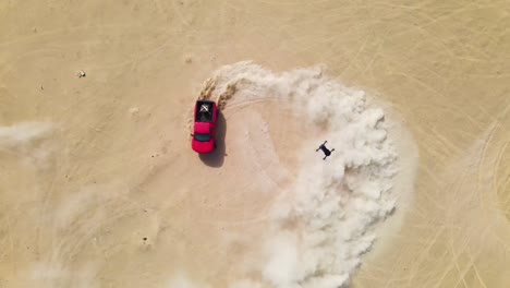 drone looking down on a red truck doing high speed doughnuts in the desert, kicking up big clouds of sand dust