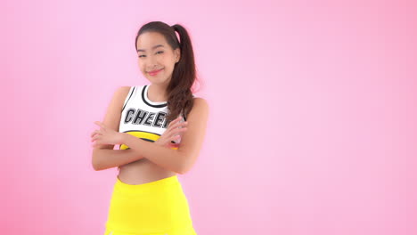 노란색 치어리더 의상을 입은 매력적인 젊은 아시아 여성이 팔과 미소를 교차합니다.