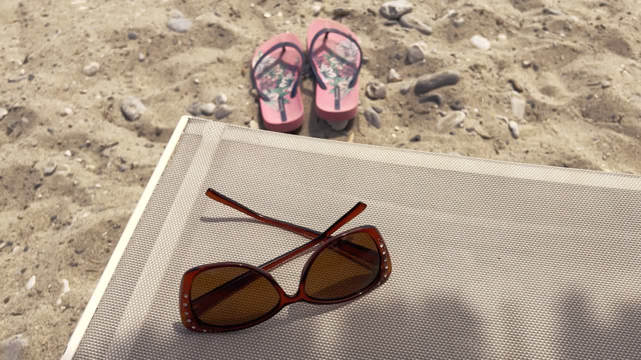 Close-up of sunglasses on sunbed and flip-flops in the sand
