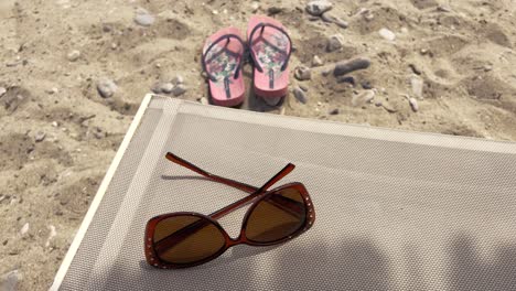 close-up of sunglasses on sunbed and flip-flops in the sand