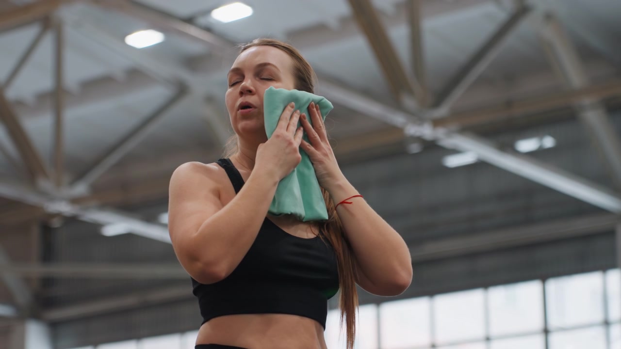 Industrial roof badminton training caucasian athlete wiping face with towel under bright ceiling lights, focused on power and endurance drills, muscular posture and determined expression in large