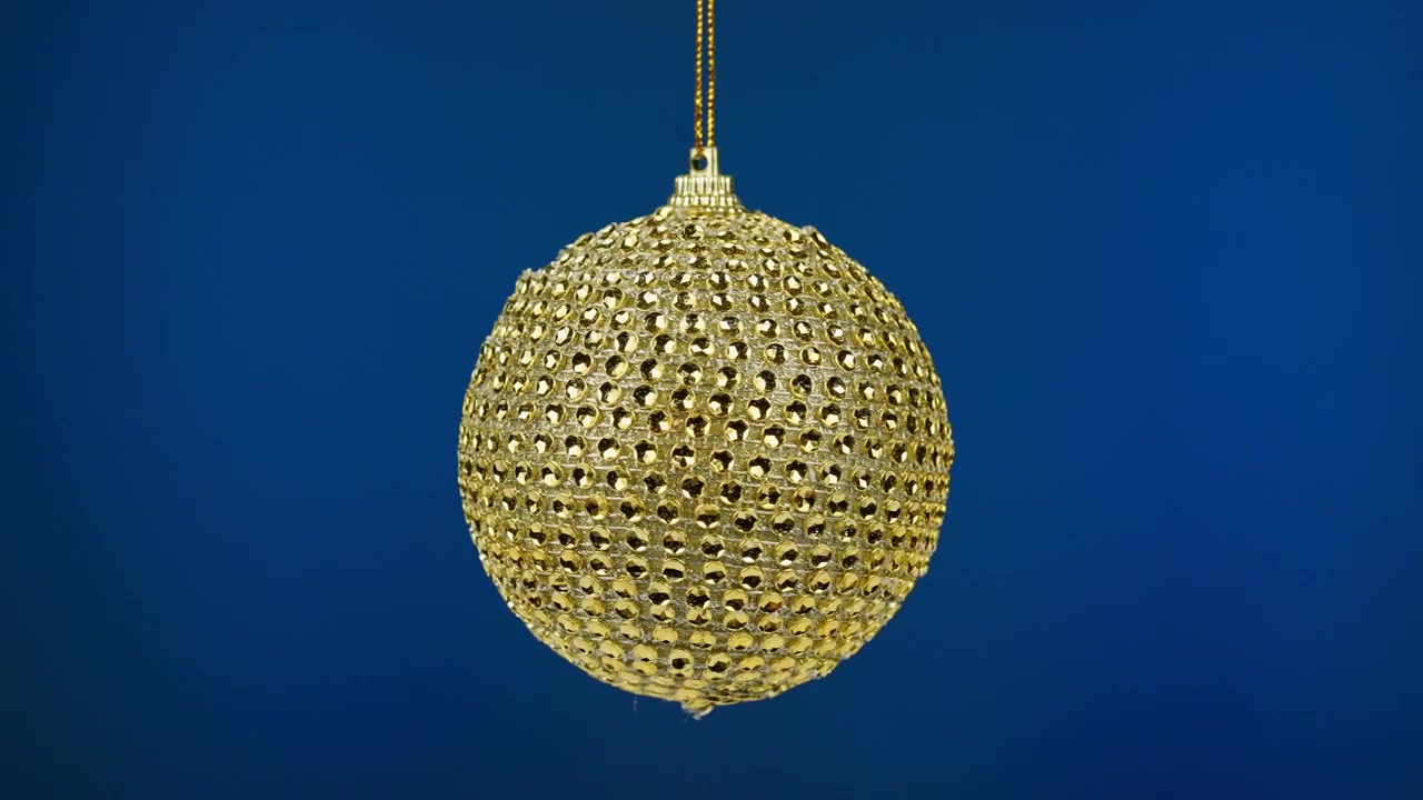 青い背景の上で回転する輝く金色のクリスマスオーナメント
