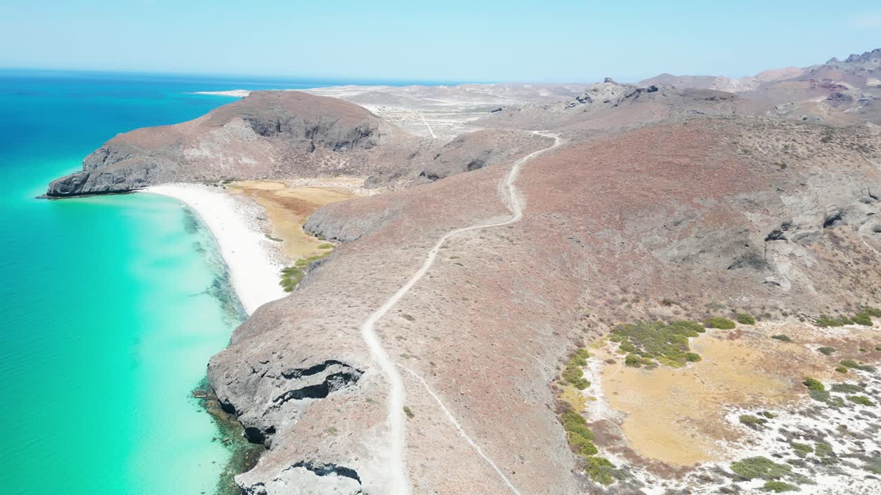 Clear blue waters, sandy coastline, and rocky mountains in Tecolandra, La Paz, Mexico