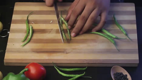 cutting green chili on a wooden chopping board by the chef in a kitchen