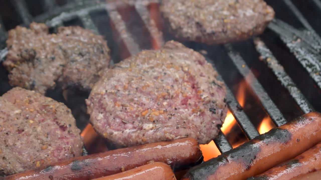 grill all'aperto primo piano di polpette di hamburger di manzo stagionato e hot dog cuocere sopra le fiamme con il fumo