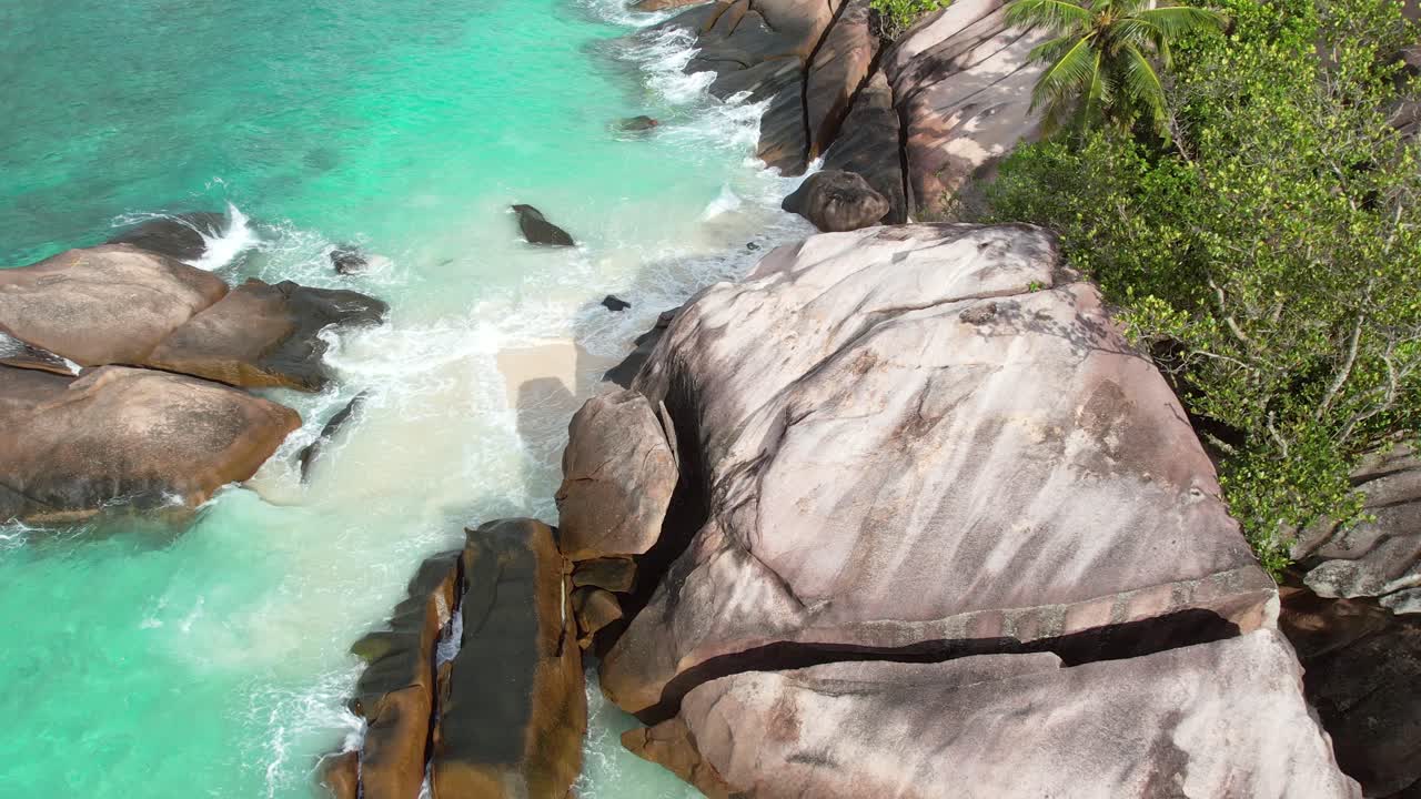 Rekaman drone yang memperlihatkan pantai berpasir putih, batu granit besar, pepohonan, dan ombak yang menghantam pantai, Mahe Seychelles 60 fps