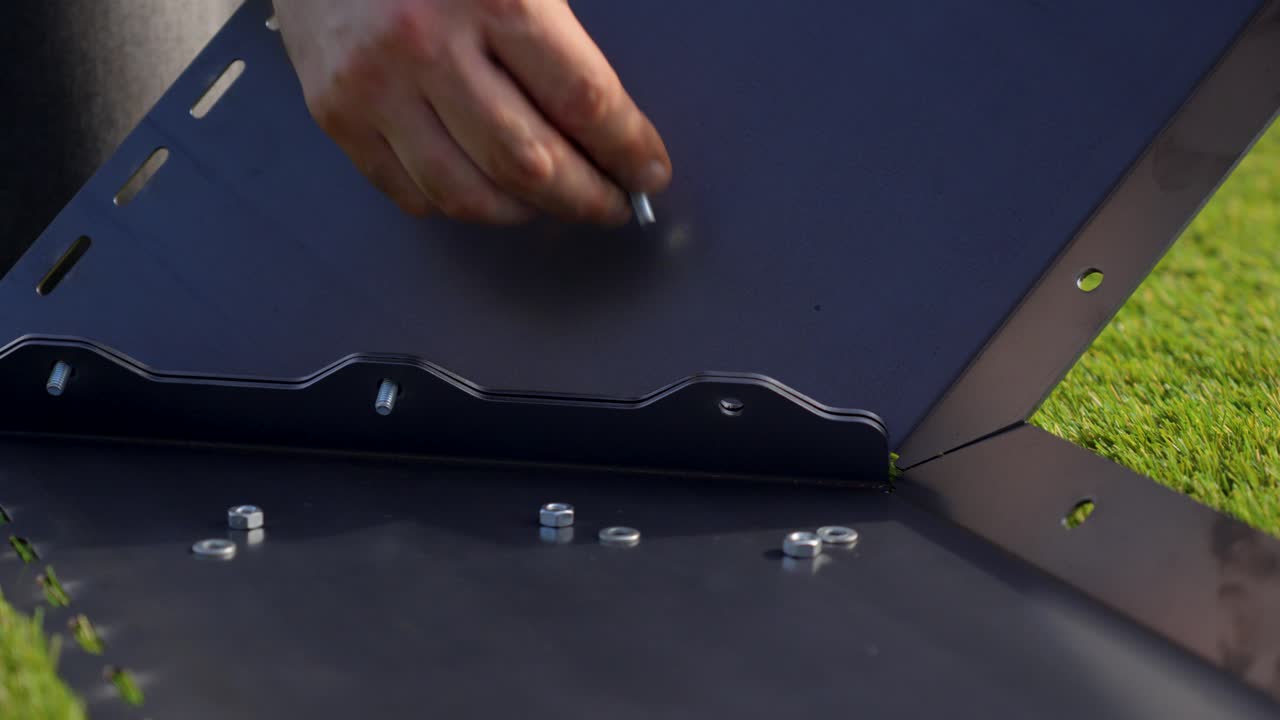 close-up of a Caucasian man's hand placing a screw into a dark, opaque metal support hole