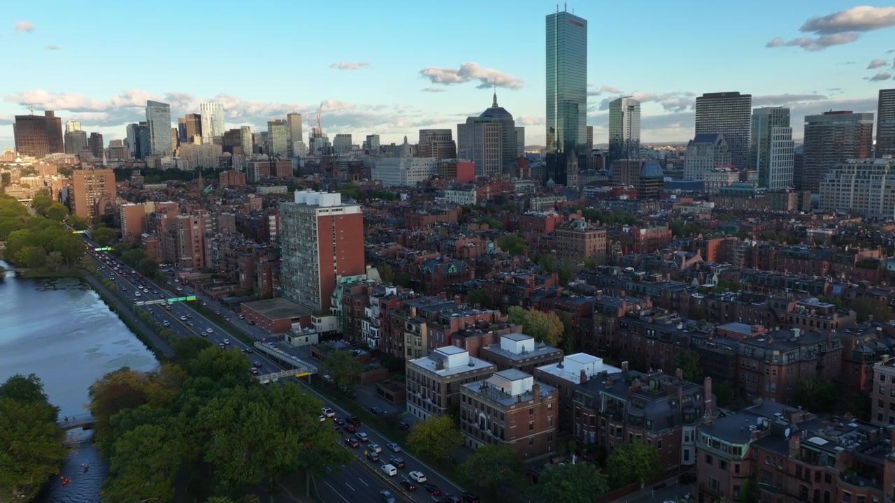 Toma de dron hacia las históricas casas de piedra rojiza de Boston y el horizonte de la ciudad, al atardecer.