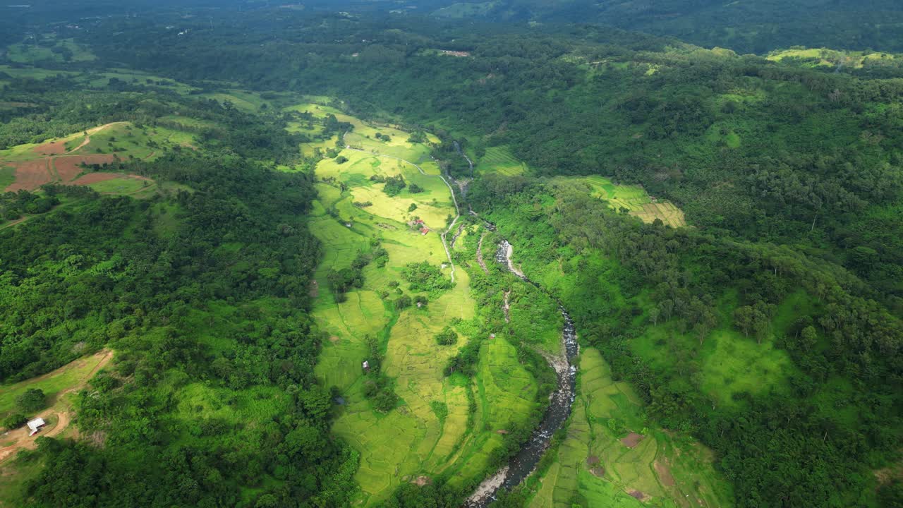 A high forward aerial of a winding river glowing under soft sunlight as it cuts through the lush valley near Quinawan Beach in Bataan, Philippines