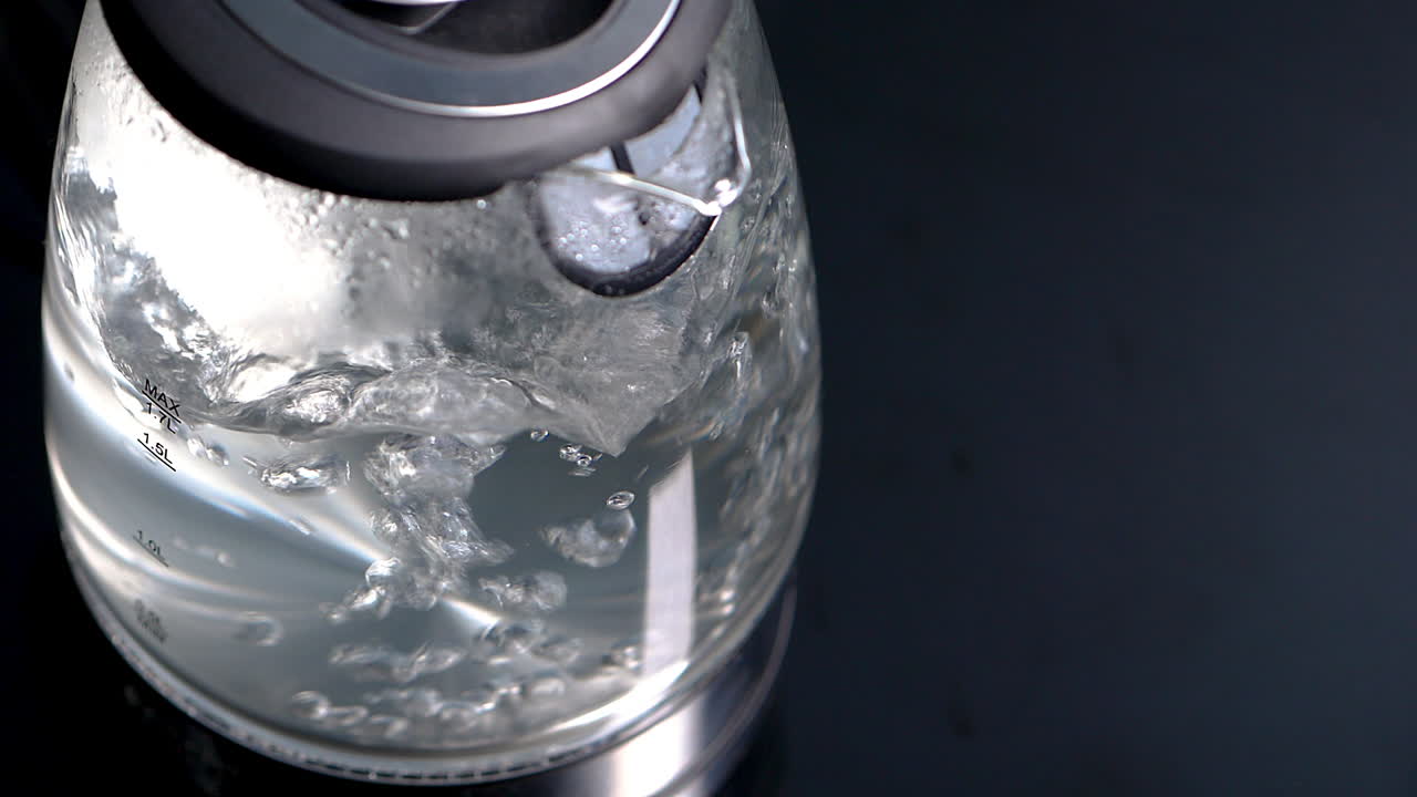 High angle of boiling water in glass kettle with visible steam, rack focus, HD