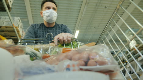 a man in a protective mask walks with a shopping trolley through the store