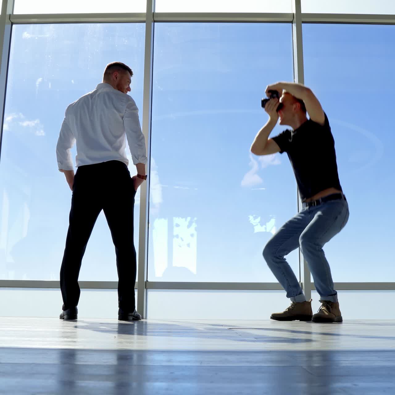 Fotografo professionista e un impiegato. Un bel ragazzo in camicia bianca e pantaloni neri in posa. Vista panoramica dalla finestra dell'ufficio su uno sfondo di cielo.