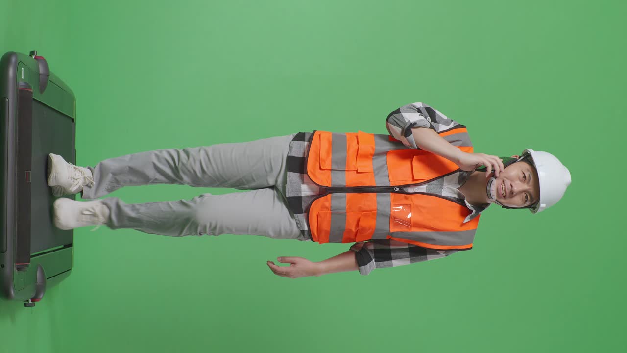 안전 헬을 입은 아시아 남성 엔지니어의 몸 전체가 녹색 화면 배경 스튜디오에서 는 동안 스마트폰으로 이야기하고 있습니다.