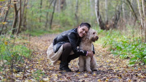 woman hugging goldendoodle in the woods and kissing her dog