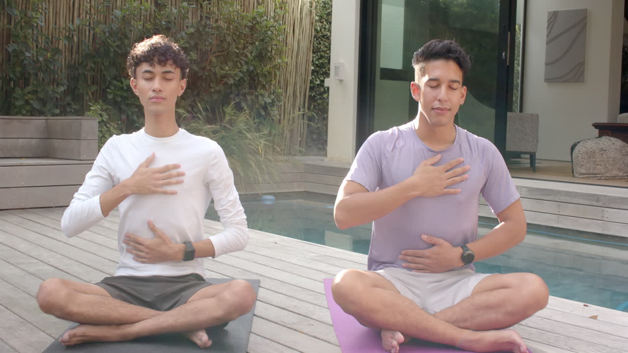 Meditating outdoors, multiracial gay couple practicing mindfulness on yoga mats by pool