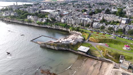 drone footage captures the st andrews coastline, tidal pools, and adjacent town under bright daylight, with smooth camera movement and wide scenic perspective