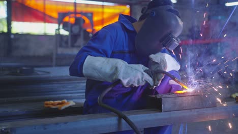 asian male technician worker in a safty uniform wear welders leathers,electric wheel grinding on steel structure in factory workshop in the garage, orange bokeh sparks fly to the sides