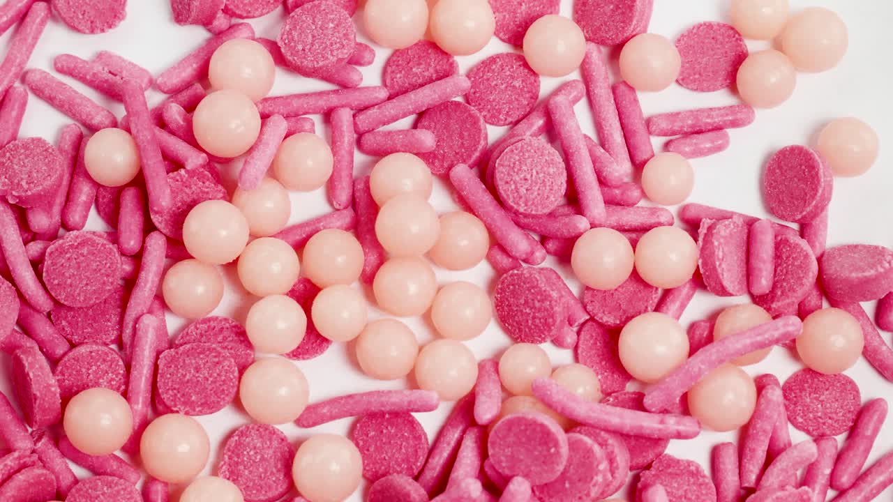 Pink and peach sprinkles cascade onto a white surface, captured in extreme close-up with bright lighting