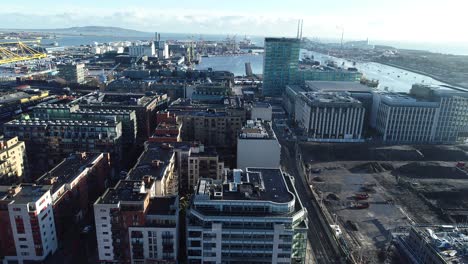 a building site in dublin, ireland with cranes above and the foundations of buildings below. the flyover shot shows newly built houses surrounding the area while construction continues.