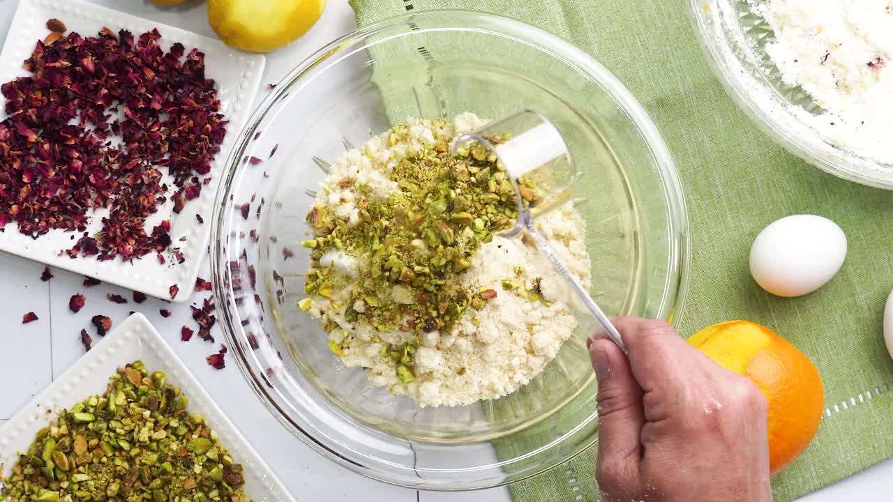 Baking a dessert called Persian Love Cake made with rose petals and pistachios. Cake with white glaze frosting. Mixing in the pistachio nuts to the batter. Beautiful cake for tea time or celebration