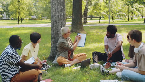 Mujer-Enseñando-A-Estudiantes-Universitarios-Multiétnicos-Al-Aire-Libre