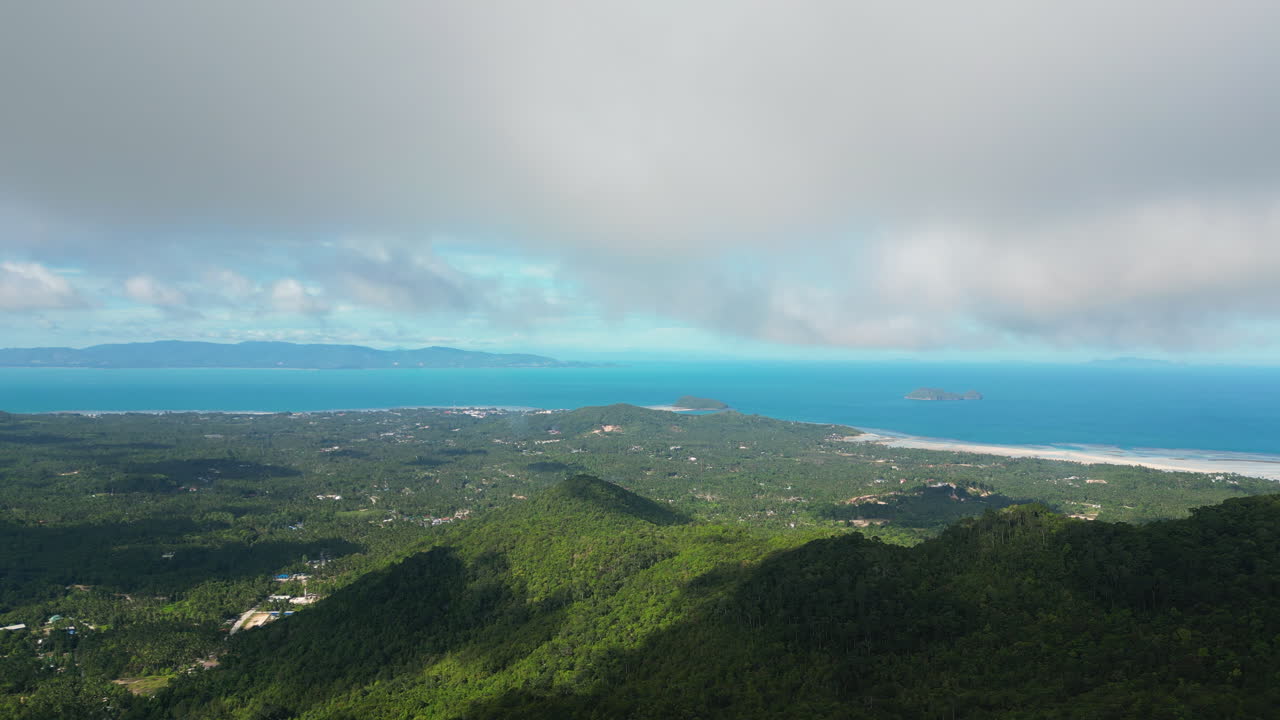Aerial wide shot over green Koh Phangan Island and blue ocean during cloudy day - panorama view