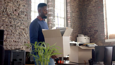 happy african american casual businessman holding box with documents in office in slow motion