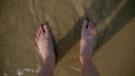 Young-man-legs-on-a-sandy-beach,-wave-washing-up