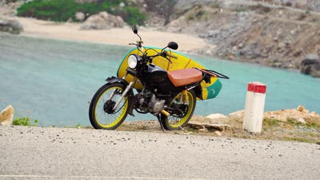 moto con tabla de surf amarilla adjunta de pie en el pie de apoyo al lado de la vista al mar