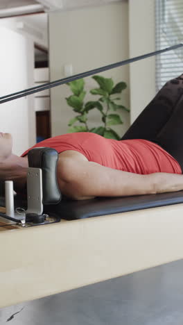 vertical video of senior caucasian woman stretching on reformer in pilates studio, slow motion