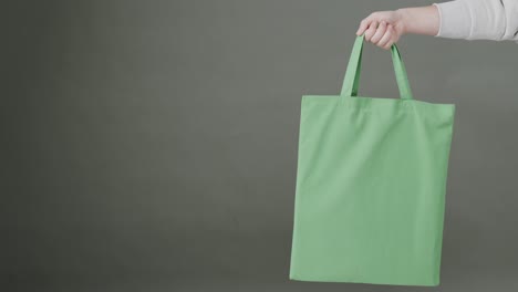 hand of caucasian woman holding green bag on grey background, copy space, slow motion