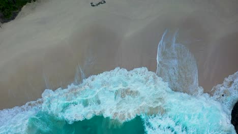 Aerial-shot-of-turquoise-ocean-waves-crashing-white-sand-coastline-of-Kelingking-Beach-with-azure-lagoon-and-T-Rex-Bay-Nusa-Penida-one-of-the-most-popular-tourist-attraction-near-island-Bali