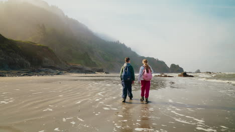 two people with backpacks walking on a foggy beach