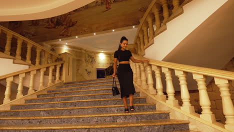 Beautiful-elegant-young-woman-wearing-a-black-dress,-walking-down-a-luxurious-staircase