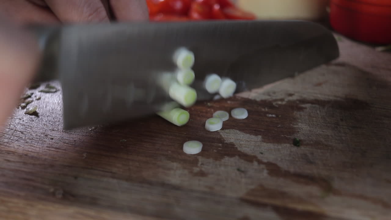 Slow pan left to right of spring onions being chopped on wooden chopping board