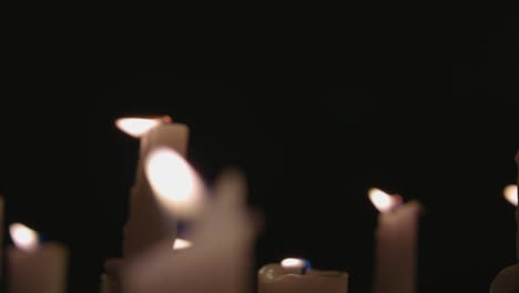 un primer plano extremo y una panorámica de velas blancas encendidas con un fondo negro