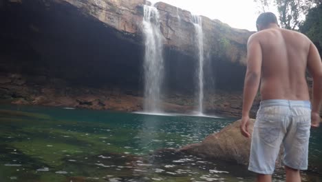 young man enjoying the natural waterfall falling from mountain top at morning video taken at krangsuri waterfall meghalaya india