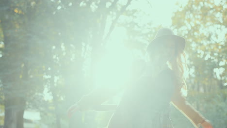 cheerful stylish caucasian young woman wearing a hat and coat spinning in the park while throwing autumn yellow leaves and looking at camera