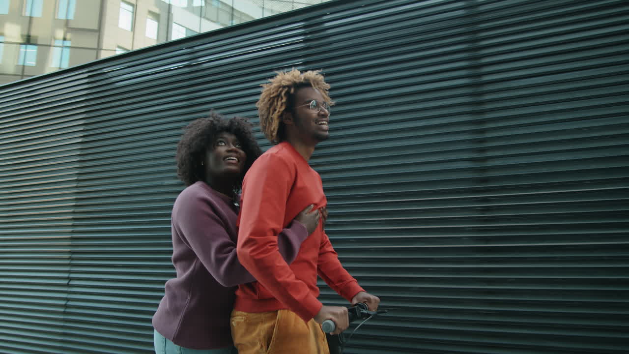 pareja afroamericana montando un scooter eléctrico juntos