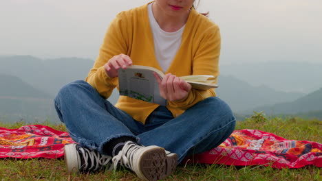 slow reveal of a woman reading a book on a windy mountaintop