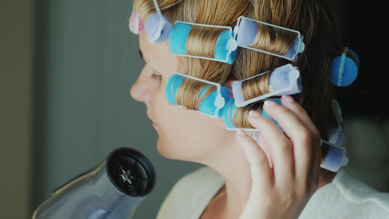 그녀의 머리에 curlers와 여자는 헤어 드라이어로 머리를 건조