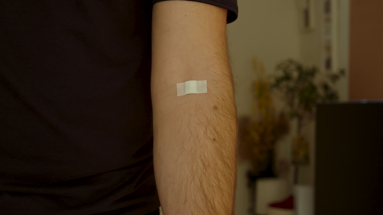 Primo piano cinematografico di una persona che mostra un piccolo cerotto adesivo sull'avambraccio dopo un'iniezione o un esame del sangue. Utile per concetti relativi a assistenza sanitaria, vaccinazione, controlli medici, recupero e benessere.