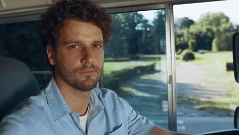 Closeup-handsome-driver-sit-in-schoolbus-cabin.-Bearded-man-looking-camera.