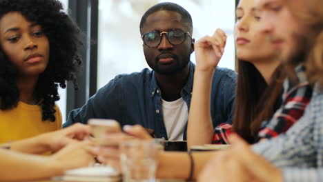 close-up view of multiethnic group of friends talking and using smartphone sitting at a table in a cafe