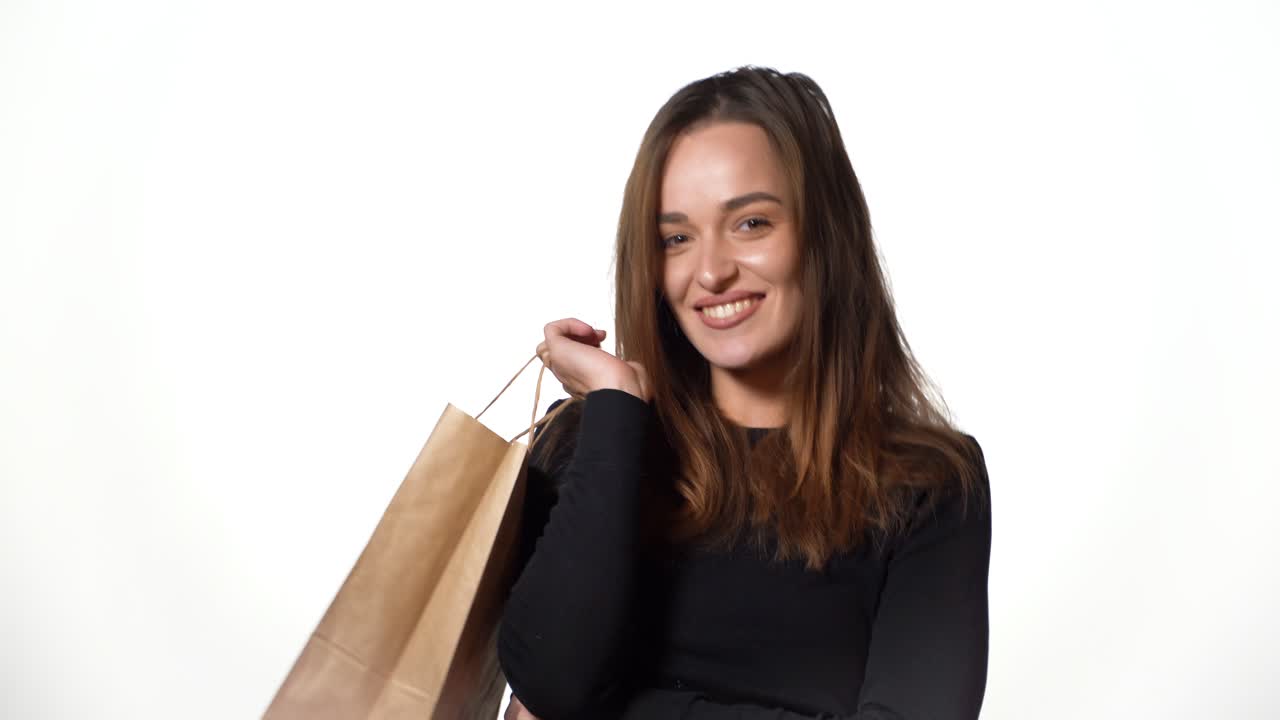 A beautiful woman in a black jumper is holding brown packages in her hands and posing with them after shopping on a white background.